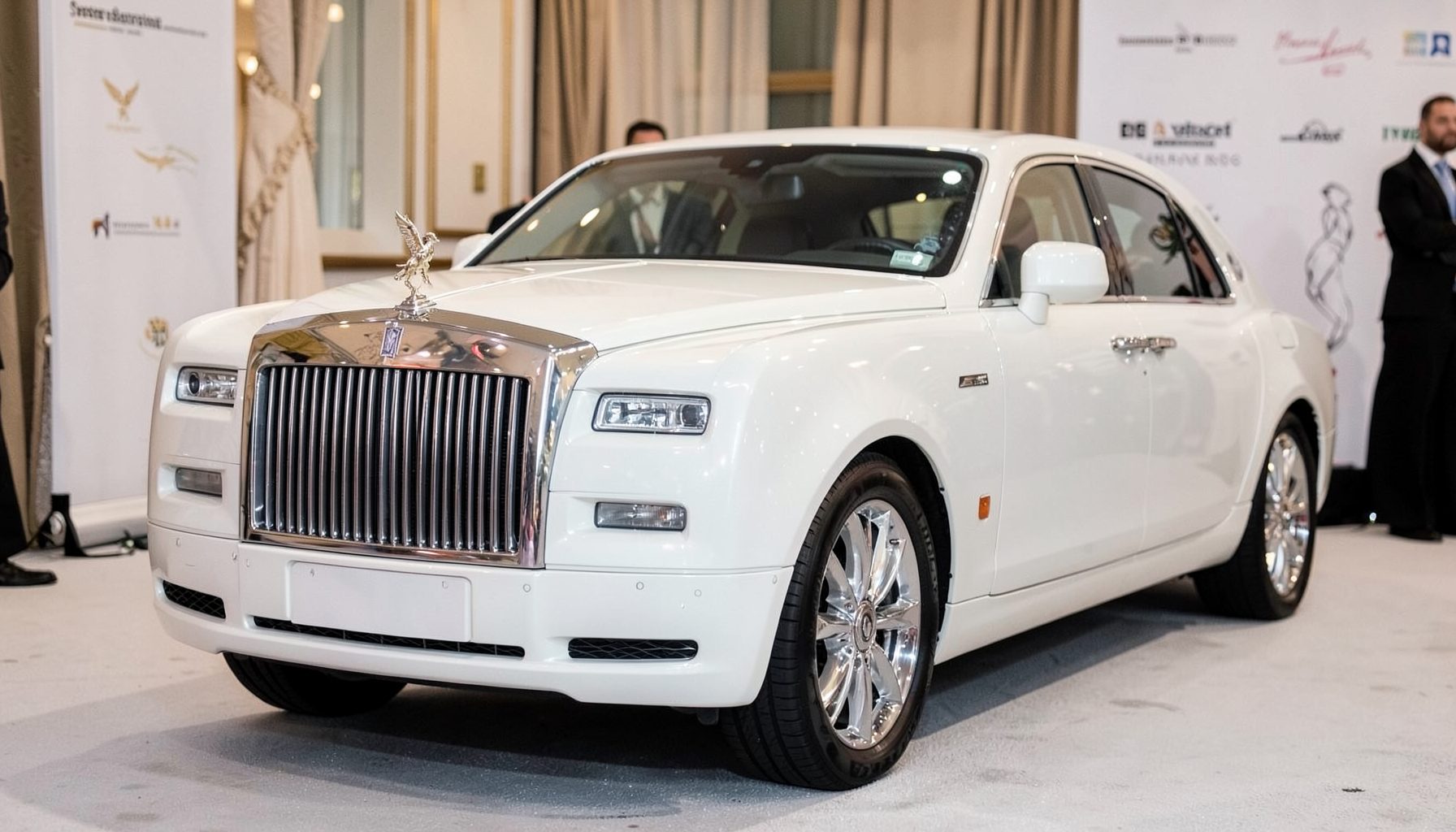 Pearlescent white Rolls Royce with iconic grille and Spirit of Ecstasy ornament, set against a formal event backdrop