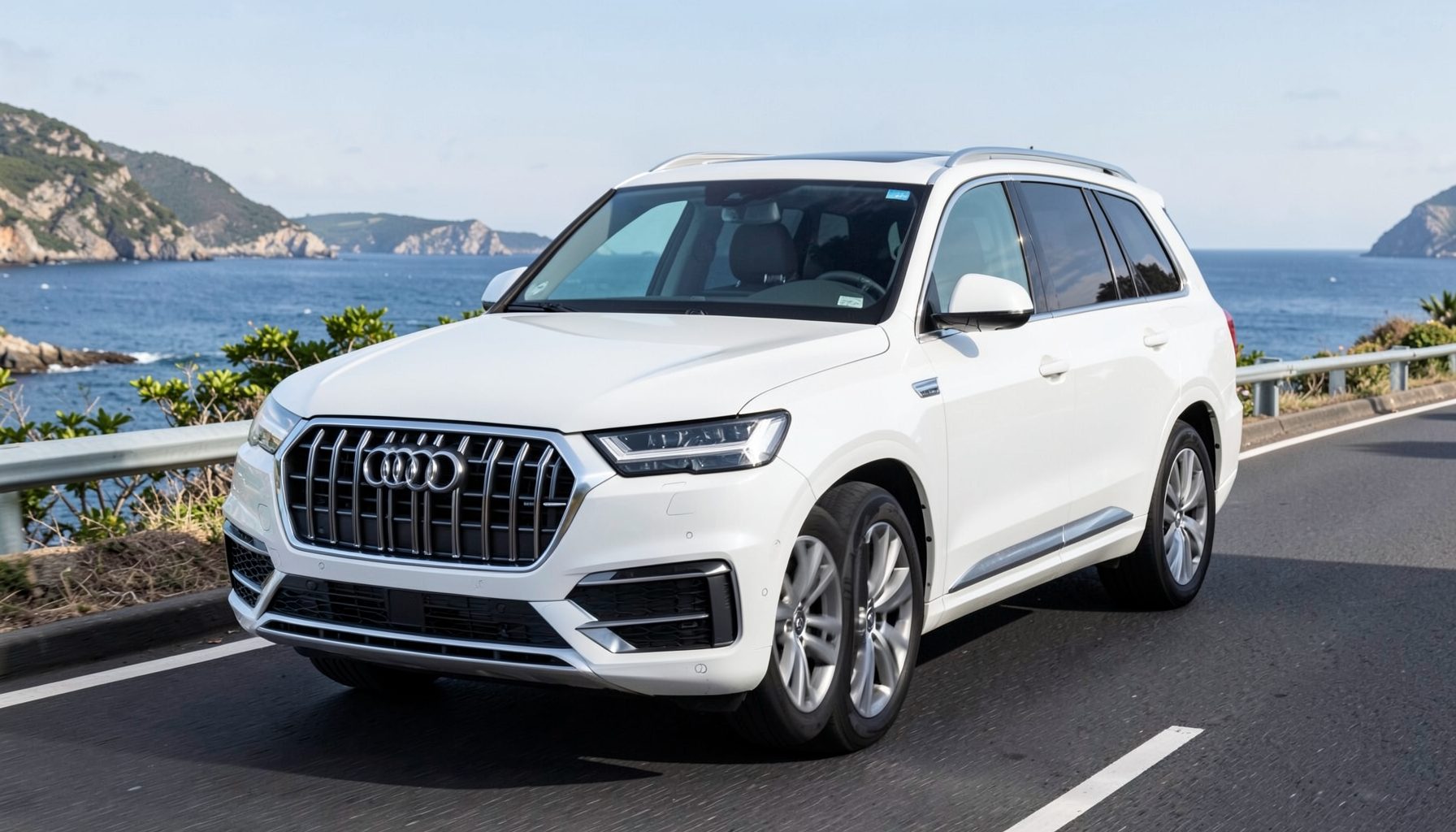 White Audi Q7 luxury SUV with bold front grille, three-row seating, shown on a scenic coastal road
